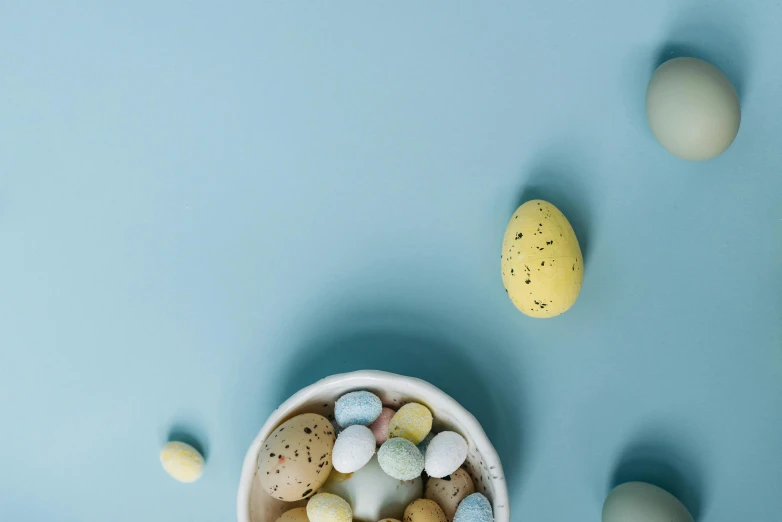 a bowl filled with eggs sitting on top of a blue surface, by Matthias Stom, trending on unsplash, candy decorations, background image