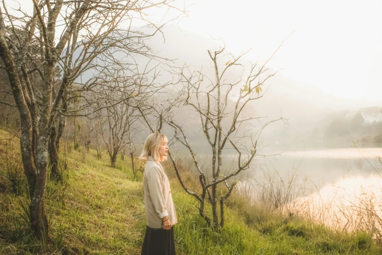 a woman standing in front of a body of water, inspired by Camille Corot, unsplash, soft warm light, valley mist, blonde, cottagecore