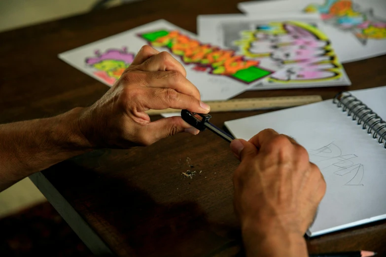 a person is drawing on a piece of paper, by Matthias Stom, pexels contest winner, process art, jim woodring, crafts and souvenirs, in a workshop, hand on table