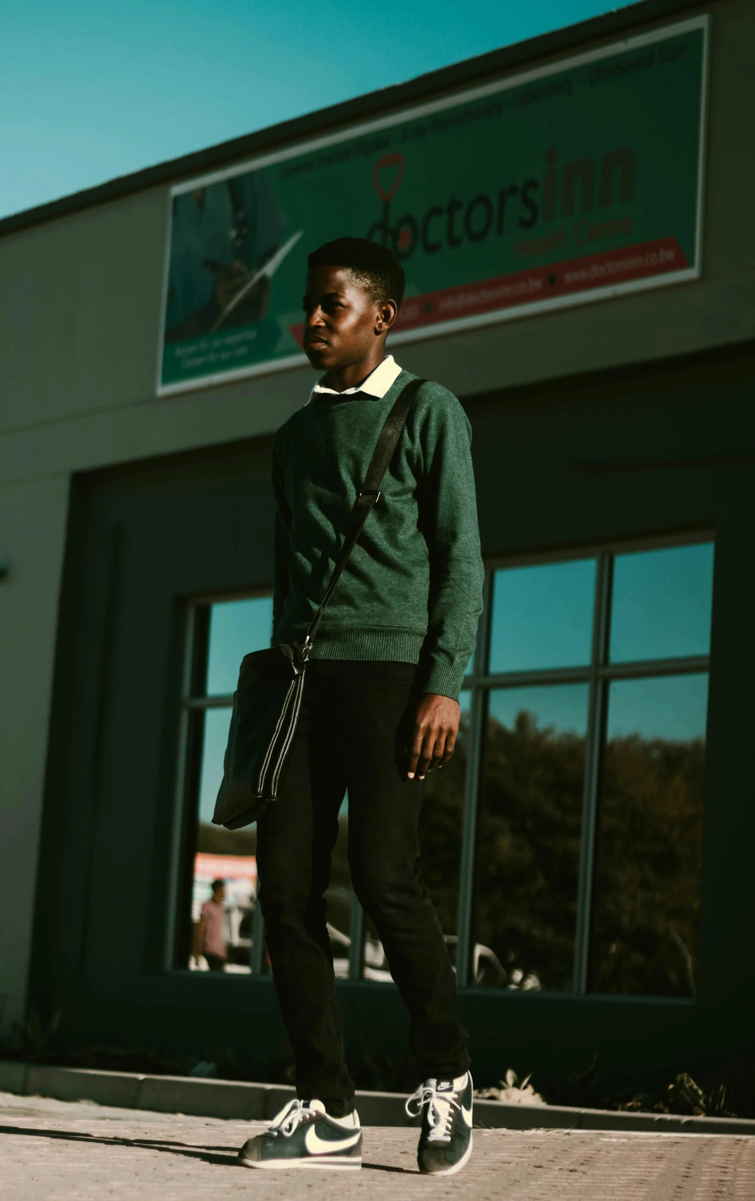 a man standing on a skateboard in front of a building, an album cover, by Maxwell Bates, pexels, happening, wearing a green sweater, mkbhd, human staring blankly ahead, 15081959 21121991 01012000 4k