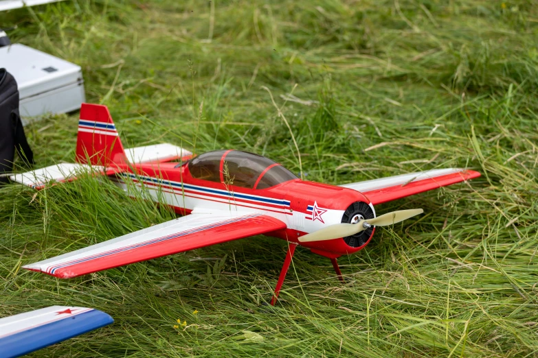 a toy airplane sitting on top of a lush green field, it has a red and black paint, aero dynamic, patriot, 300mm