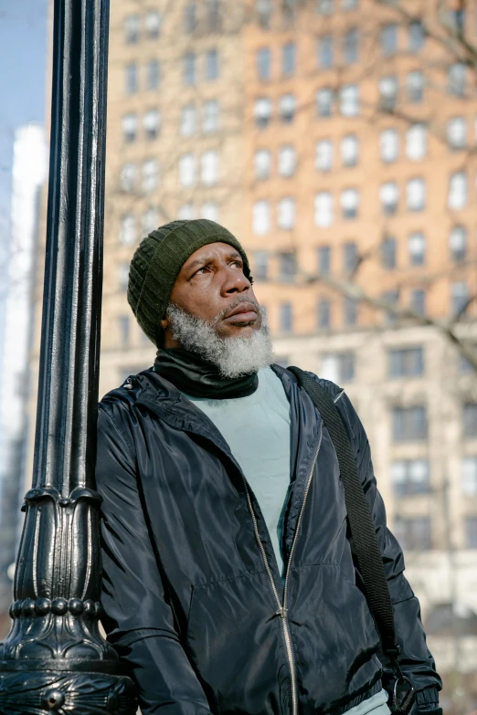 a man standing next to a lamp post in a city, inspired by Gordon Parks, trending on pexels, he also wears a grey beanie, morgan freeman, square, humans of new york