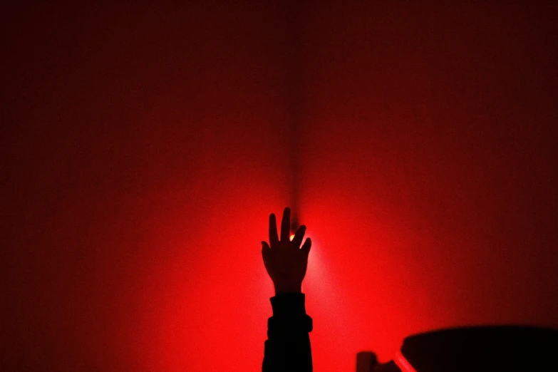 a person standing in front of a red light, symbolism, raised hand, dramatic lighting from below, photographed for reuters, some red