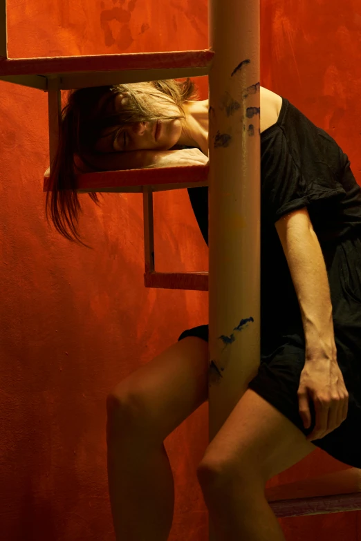 a woman in a black dress leaning against a pole, inspired by Nan Goldin, hyperrealism, red room, movie still of a tired, cardboard, promotional image