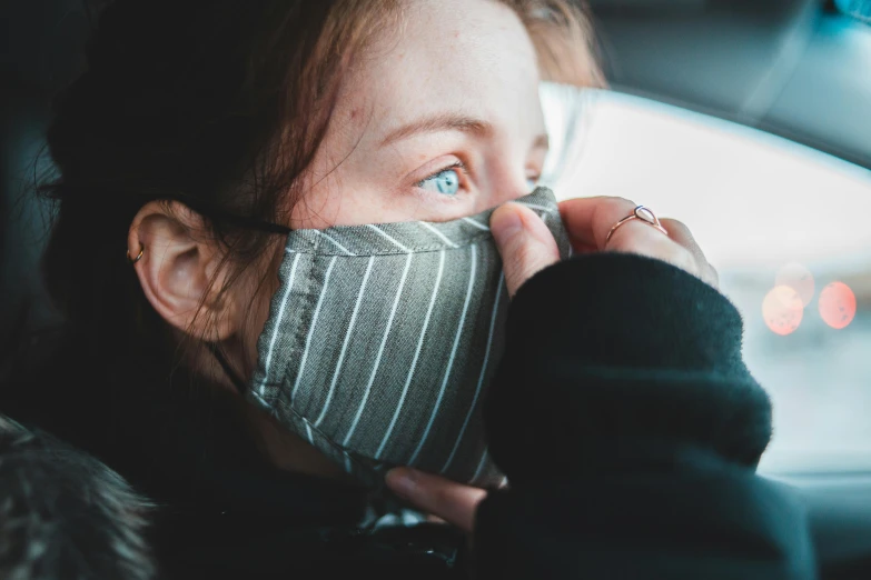 a woman in a car wearing a face mask, a picture, by Emma Andijewska, trending on pexels, stripe over eye, sick with a cold, grey, bottom angle