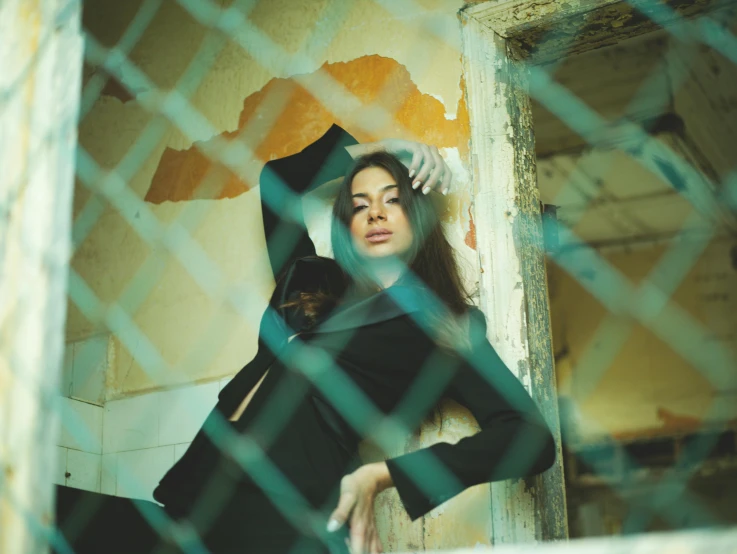 a woman leaning against a wall behind a chain link fence, a picture, inspired by Elsa Bleda, pexels contest winner, arabesque, young arab monica bellucci, standing in abandoned building, with instagram filters, anna nikonova aka newmilky