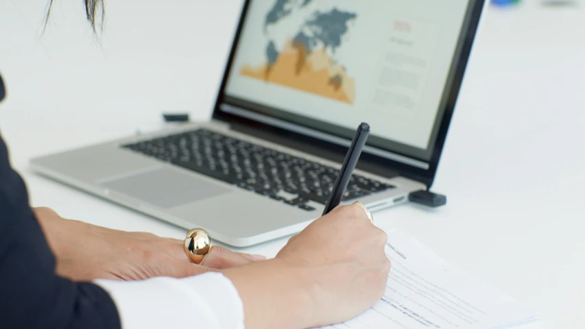 a woman writing on a piece of paper in front of a laptop, a digital rendering, by Alison Watt, trending on unsplash, thin gold details, government archive, highly detailed rounded forms, it specialist