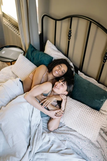 a couple of women laying on top of a bed, trending on pexels, non-binary, indoor picture, seasonal, woman holding another woman