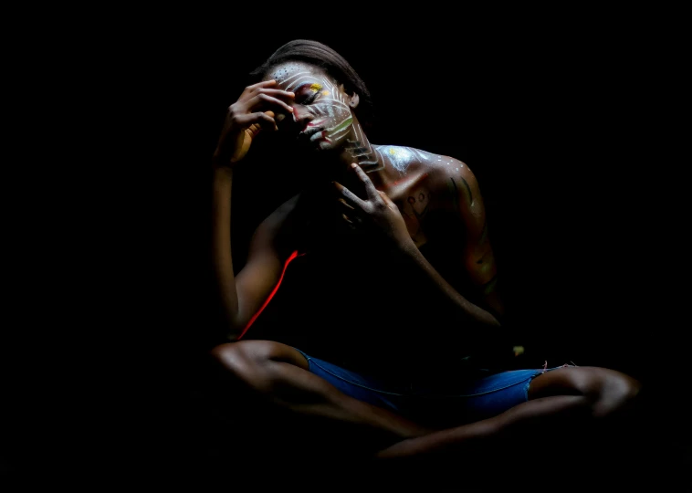 a man with painted face sitting in the dark, by Lily Delissa Joseph, pexels contest winner, art photography, african woman, lascivious pose, aboriginal art, !!! colored photography
