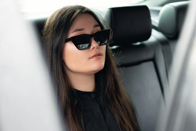 a woman sitting in the back seat of a car, inspired by Ion Andreescu, wearing shades, young woman with long dark hair, square, press shot