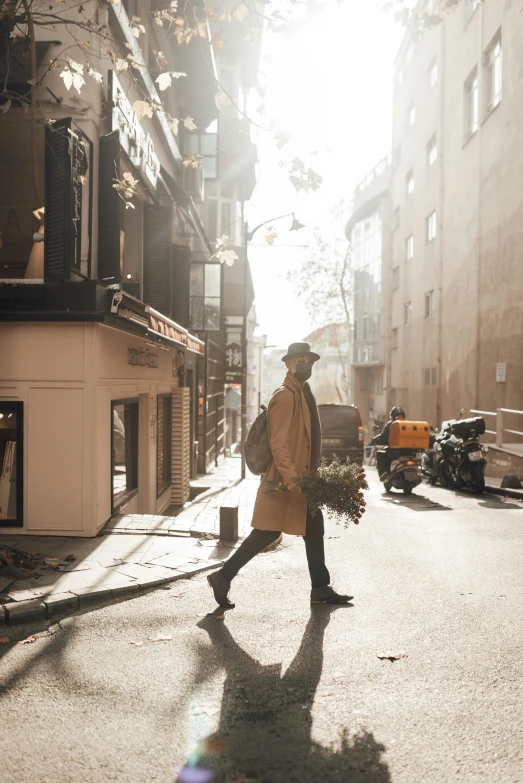 a man walking down a street next to tall buildings, pexels contest winner, romanticism, carrying flowers, light brown trenchcoat, istanbul, golden glow