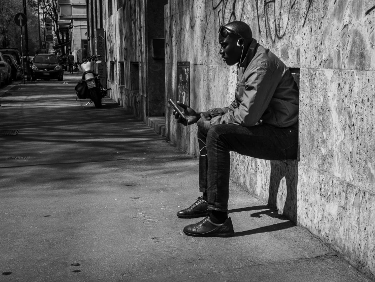 a man sitting on a bench using a cell phone, a black and white photo, by Alessandro Allori, pexels, street art, with head phones, man is with black skin, sittin