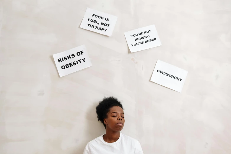 a woman sitting in front of a wall with signs on it, by Arabella Rankin, trending on pexels, on a white table, medical labels, weightlessness, black young woman