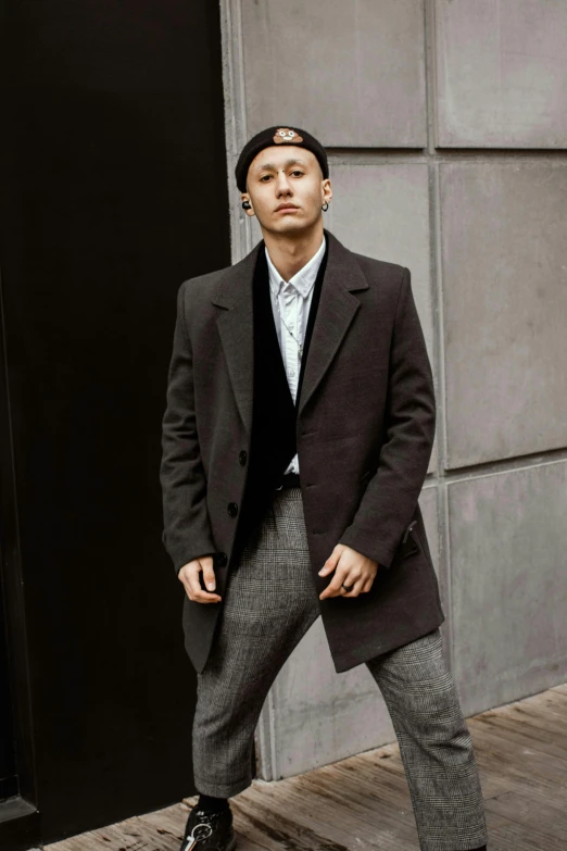 a man in a suit and tie standing in front of a building, an album cover, inspired by Joong Keun Lee, trending on pexels, renaissance, grey turtleneck coat, he is wearing a black trenchcoat, non binary model, a suited man in a hat