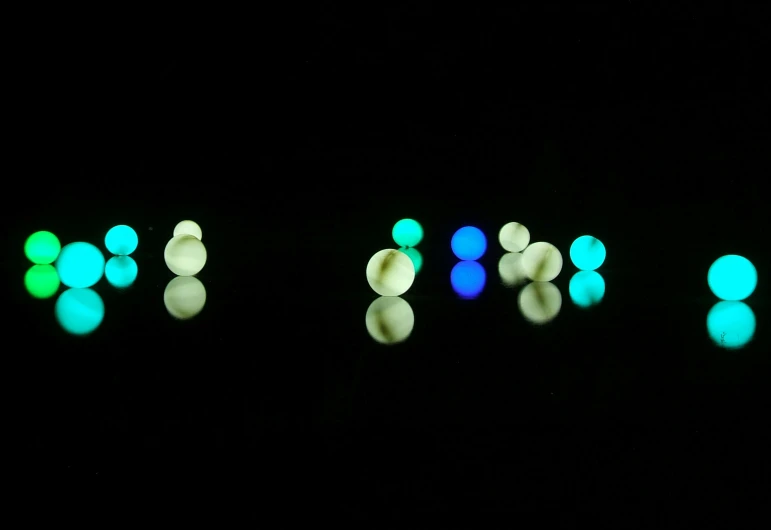 a group of balls sitting on top of a black surface, a microscopic photo, inspired by Bruce Munro, minimalism, blue and green light, lumen reflections, floating. greenish blue, pearls