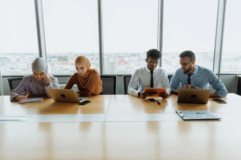 a group of people sitting around a table with laptops, trending on pexels, hurufiyya, modest, background image, engineering, 2 0 0 0's photo