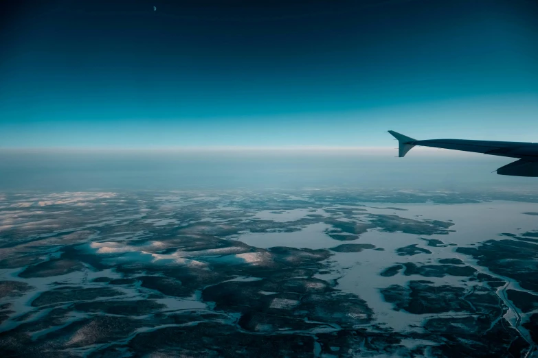 an airplane wing flying over a body of water, by Jesper Knudsen, pexels contest winner, hurufiyya, cold hues, nordic landscape, thumbnail, earth in the sky