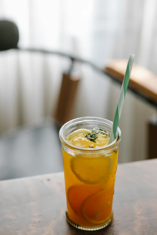 a drink sitting on top of a wooden table, a picture, unsplash, trapped in tall iced tea glass, thumbnail, yellow, grey orange