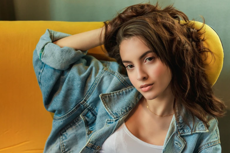 a beautiful young woman sitting on top of a yellow chair, inspired by Elsa Bleda, trending on pexels, photorealism, denim jacket, no makeup wavy hair, beautiful face and flawless skin, laying down