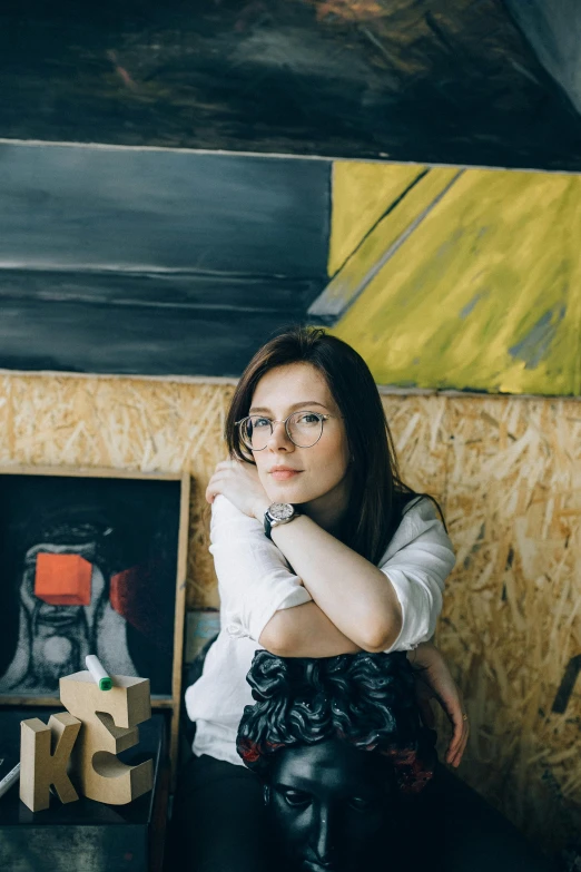 a woman sitting on a bench in front of a painting, a portrait, by Grytė Pintukaitė, pexels contest winner, arbeitsrat für kunst, girl with glasses, engineer, in a workshop, on a yellow canva