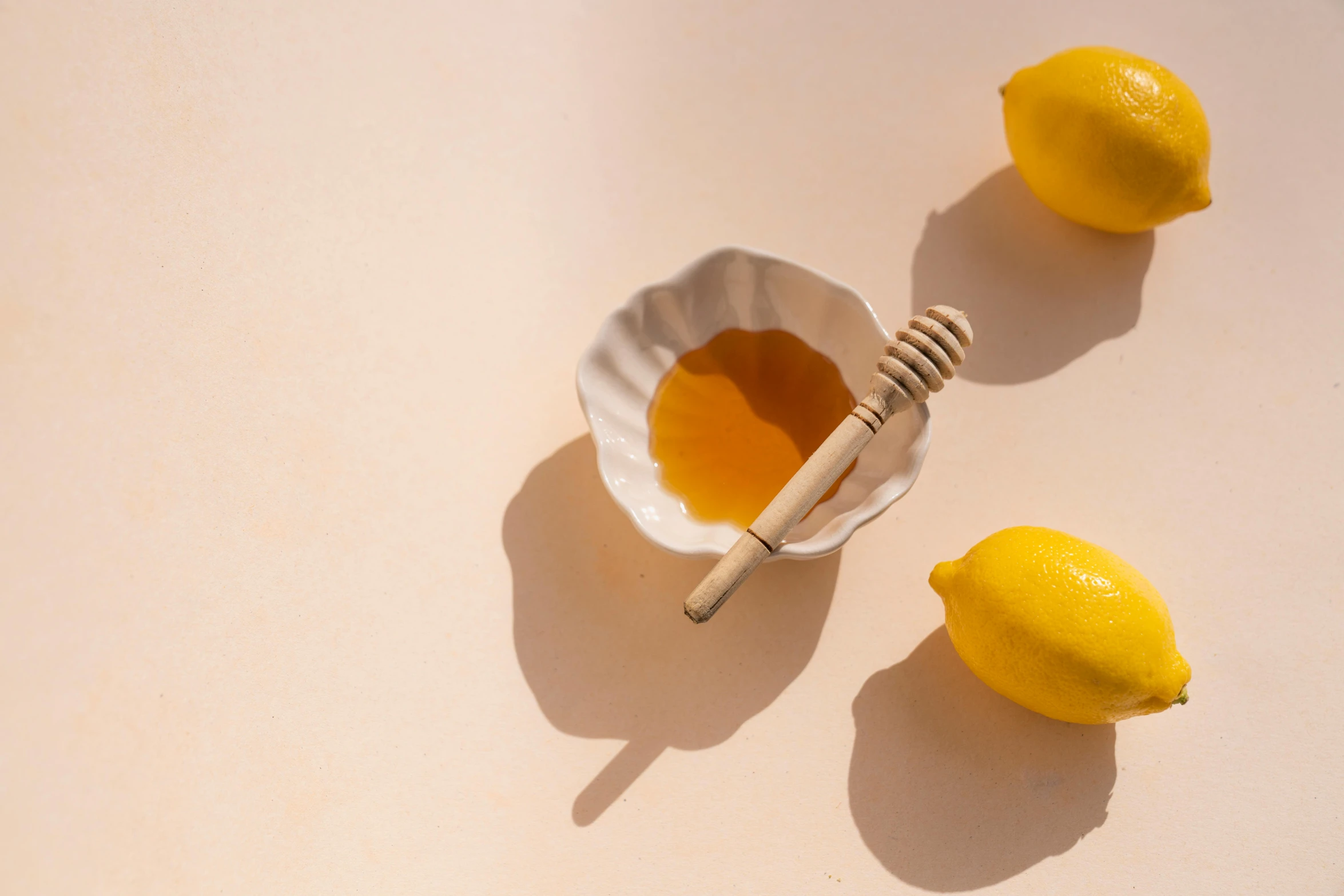 a bowl of honey and lemons on a table, by Nicolette Macnamara, trending on unsplash, minimalism, sunbathed skin, spoon placed, glaze, on a pale background