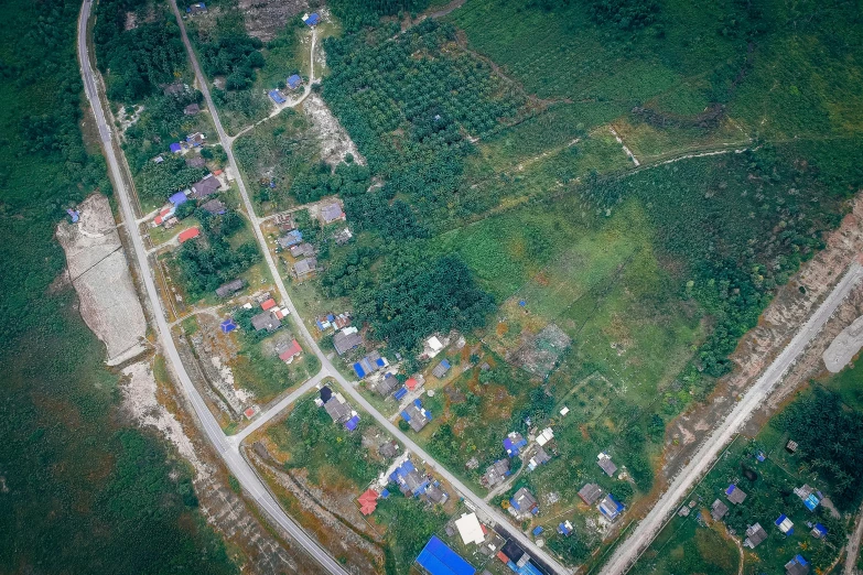 an aerial view of a small town surrounded by trees, sumatraism, background image, pengzhen zhang, color image, makeshift houses