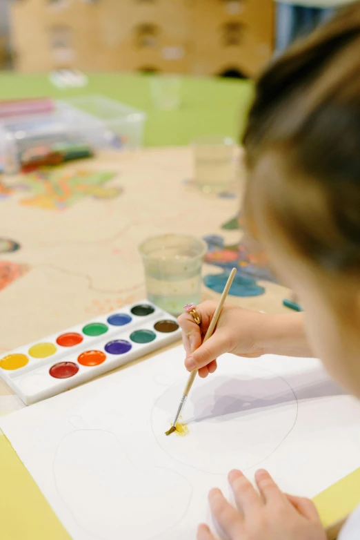 a little girl is painting on a piece of paper, trending on pexels, process art, watercolors on canvas, subject in the centre, palette of primaries, painting on a badge