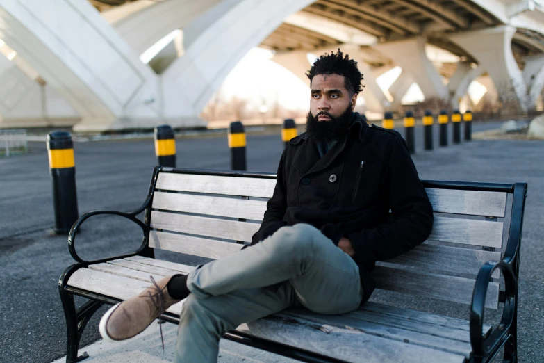 a man sitting on top of a wooden bench, by Washington Allston, pexels contest winner, black curly beard, model wears a puffer jacket, grey pants and black dress shoes, jaylen brown
