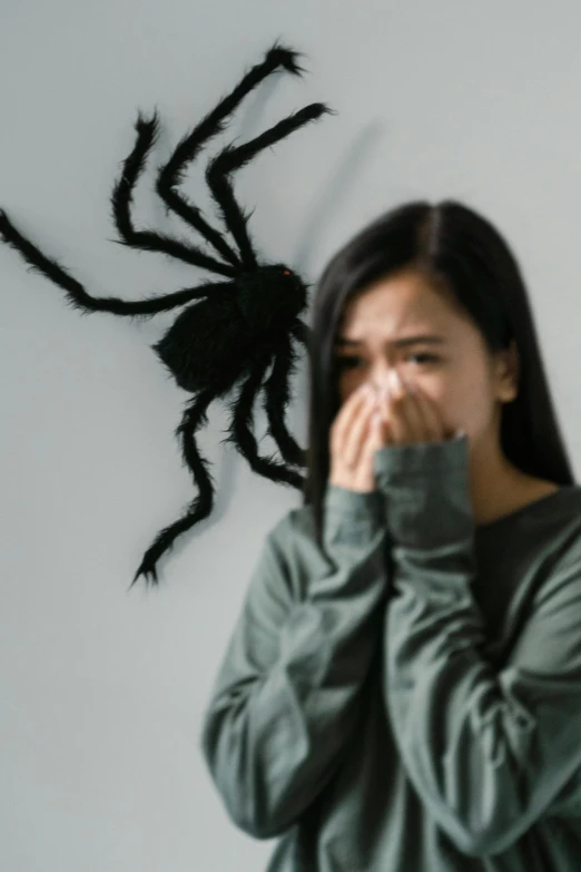 a woman covering her mouth in front of a fake spider, antipodeans, a young asian woman, coughing, anxiety environment, a dark