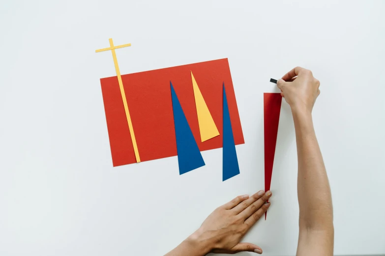 a person holding a piece of paper with a cross on it, inspired by Alexander Calder, unsplash, interactive art, asymmetrical spires, wall mural, primary colours, sail