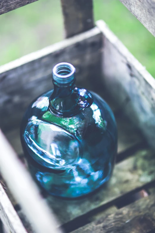 a blue glass bottle sitting inside of a wooden crate, inspired by Elsa Bleda, unsplash, renaissance, green water, al fresco, prussian blue, wine