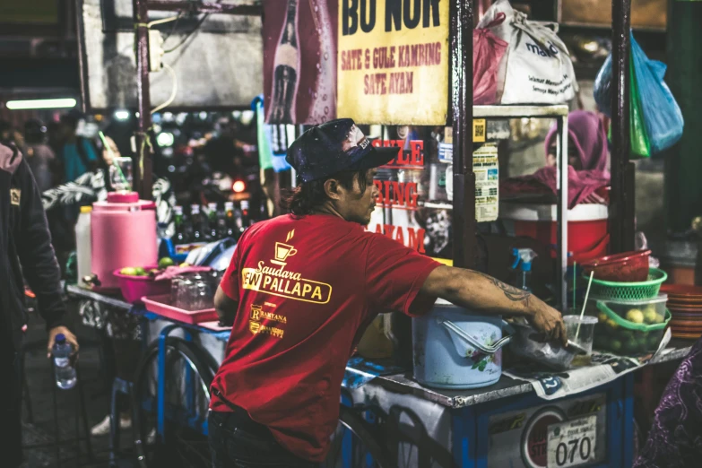 a man in a red shirt standing in front of a food stand, a silk screen, pexels contest winner, thai, neon signs, avatar image, maintenance photo