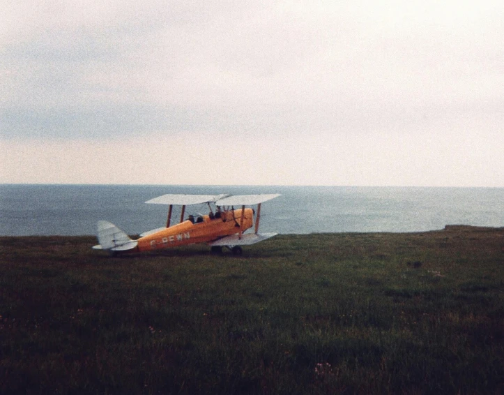 a small plane sitting on top of a lush green field, a colorized photo, by Attila Meszlenyi, hurufiyya, near the sea, vintage aesthetic, hopper, 90's photo