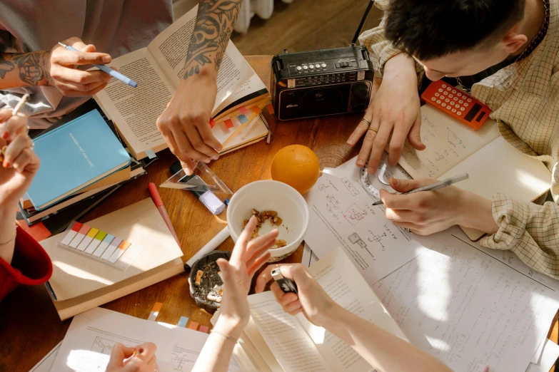 a group of people sitting around a wooden table, a drawing, trending on pexels, flatlay book collection, sharpie, college students, character sheets on table