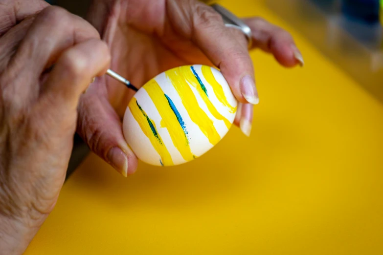a close up of a person holding a painted egg, an airbrush painting, inspired by Károly Markó the Elder, pexels contest winner, stripes, yellow, ornament, recipe