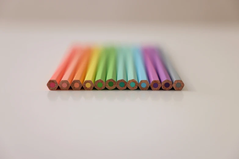 a row of colored pencils sitting on top of a table, by Rachel Reckitt, pexels, crayon art, iridescent titanium, minimalist photorealist, taken in the late 2010s, on a pale background