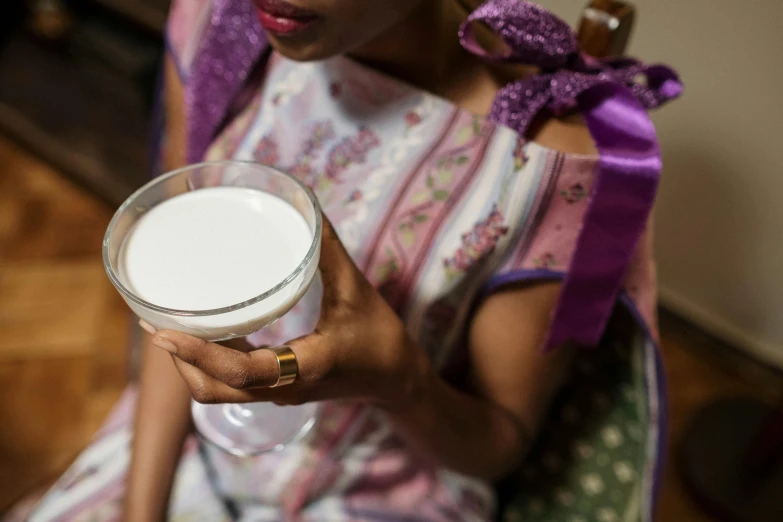 a woman sitting in a chair holding a glass of milk, unsplash, madagascar, multiple stories, closeup - view, aida muluneh