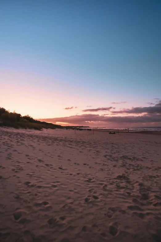 a man flying a kite on top of a sandy beach, during a sunset, beach on the outer rim, craigville, which shows a beach at sunset