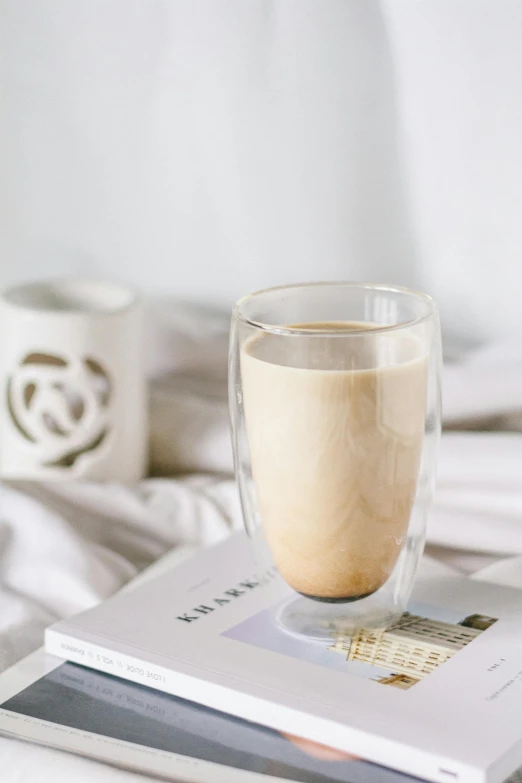 a book sitting on top of a bed next to a cup of coffee, vanilla smoothie explosion, thumbnail, glassware, beige