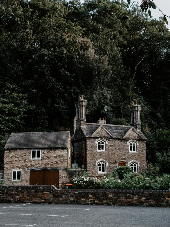 a large brick building sitting on the side of a road, by IAN SPRIGGS, pexels contest winner, cottage in the forest, chimneys, thumbnail, grey