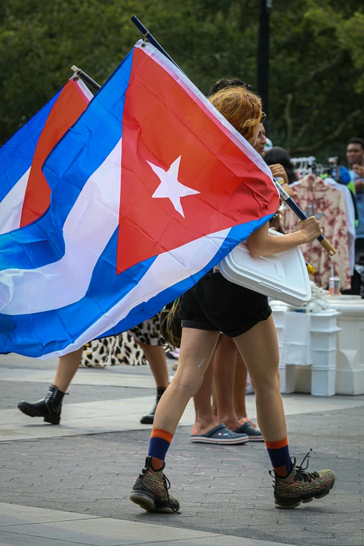 a woman walking down a street holding a cuba flag, flickr, happening, daniel libeskind, square, in 2 0 1 5, parade floats