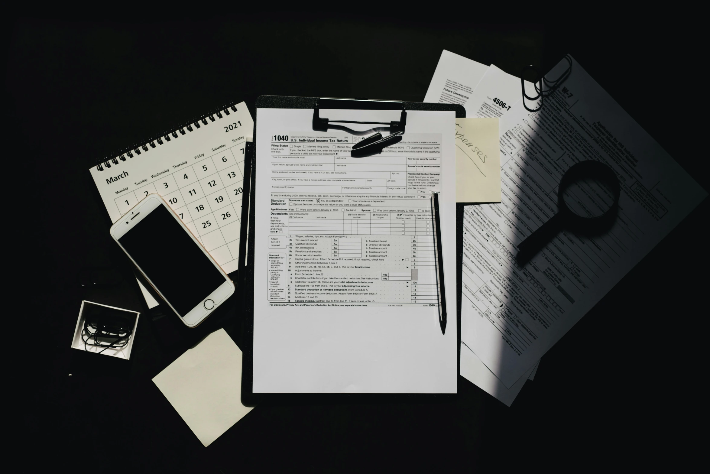 a clipboard sitting on top of a table next to papers, by Matt Cavotta, pexels contest winner, with a black background, background image, knolling, taken on iphone 14 pro