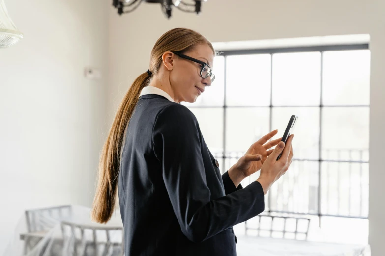 a woman in glasses looking at her cell phone, trending on pexels, wearing a black suit, worksafe. instagram photo, with a ponytail, girl wearing uniform