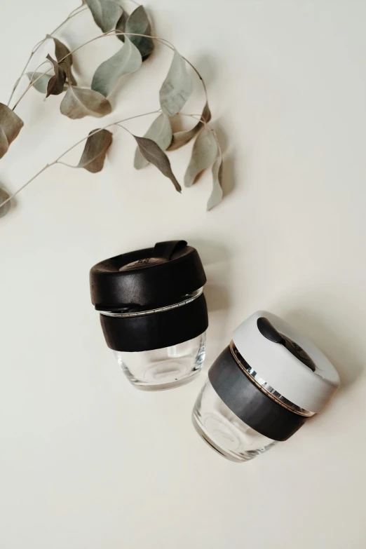 a couple of cups sitting on top of a table, product image, sustainable, white and black, glass jar