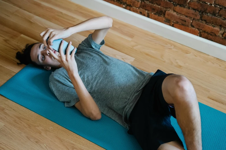 a man laying on a yoga mat using a cell phone, by Carey Morris, trending on pexels, avatar image, male teenager, blank, girl making a phone call