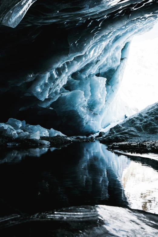 a cave filled with lots of ice next to a body of water, unsplash contest winner, surrealism, reflective surface, black, blue, antarctic