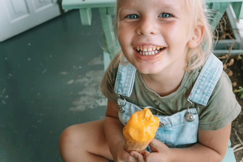 a little girl sitting on a chair holding an ice cream cone, pexels contest winner, yellow overall, manuka, thumbnail, 15081959 21121991 01012000 4k