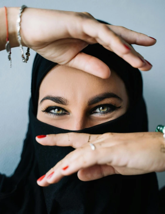 a woman wearing a black veil covering her face, an album cover, by Hedi Xandt, trending on unsplash, hurufiyya, arabian wrestling woman, making eye contact, hands shielding face, tourist photo