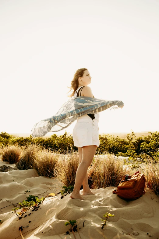 a woman standing on top of a sandy beach, wearing a towel, denim, gossamer wings, carrying survival gear