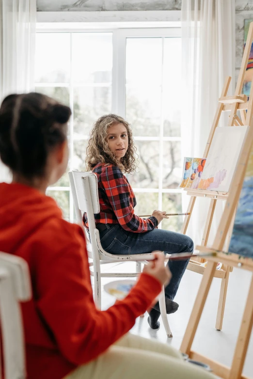 a woman sitting on a chair in front of a painting easel, a painting, pexels contest winner, a painting of two people, trending on artstion, children painting, female emo art student